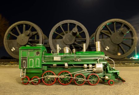 Foto de Modelo de locomotora de vapor verde con ruedas rojas delante de un conjunto de ruedas de locomotora de vapor antiguas. - Imagen libre de derechos