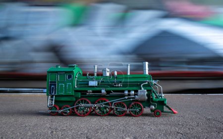 Foto de Modelo de locomotora de vapor verde con ruedas rojas con un movimiento de tren en el fondo. - Imagen libre de derechos