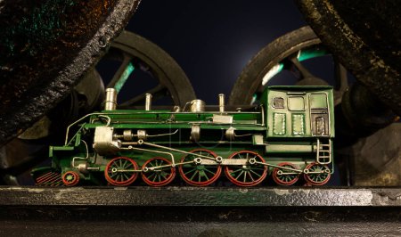 Foto de Modelo de locomotora de vapor verde con ruedas rojas bajo un juego de viejas ruedas de locomotora de vapor. - Imagen libre de derechos
