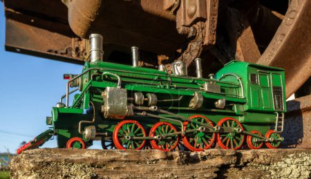 Foto de Modelo de locomotora de vapor verde con ruedas rojas bajo un vagón ferroviario. - Imagen libre de derechos