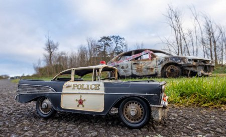 Foto de Modelo de un viejo coche de la policía investigando en un coche quemado. - Imagen libre de derechos