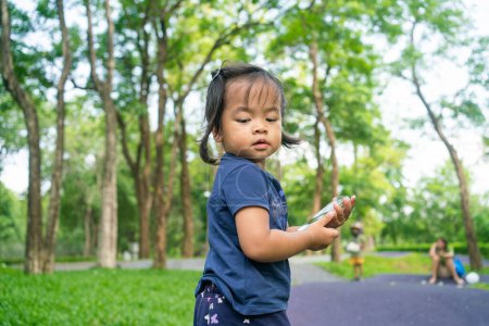 Téléchargez les photos : Portrait de heureux asiatique tout-petit fille marche dans la ville public arbre parc activité de plein air - en image libre de droit