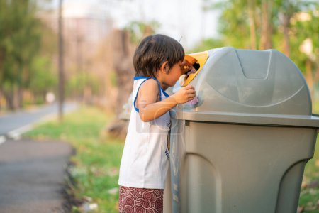 Photo for Young Asian boy carry garbage cleaning the surroundings throw trash into a bin in public park - Royalty Free Image
