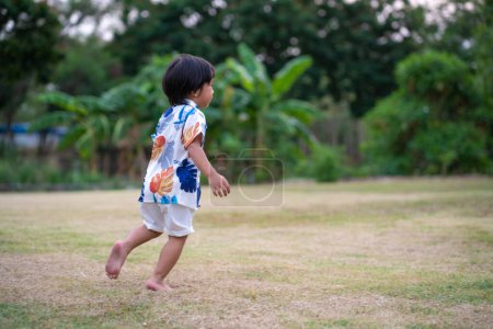 Foto de Retrato de feliz sonriente chico asiático riendo verde parque al aire libre con fondo de jardín verde borroso, juego de niños en verano. - Imagen libre de derechos