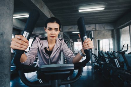 Téléchargez les photos : Femme asiatique sportive travaillant sur une machine elliptique dans une salle de gym, exercice cardio - en image libre de droit