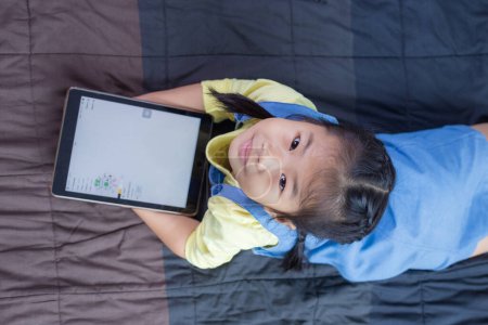Photo for Asian elementary school children using digital tablet online classroom lying on bed - Royalty Free Image