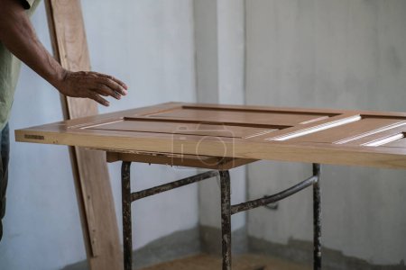 Téléchargez les photos : Charpentier travaillant avec installation de porte en bois de teck dans une nouvelle maison moderne - en image libre de droit