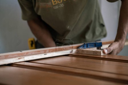 Téléchargez les photos : Charpentier travaillant avec installation de porte en bois de teck dans une nouvelle maison moderne - en image libre de droit