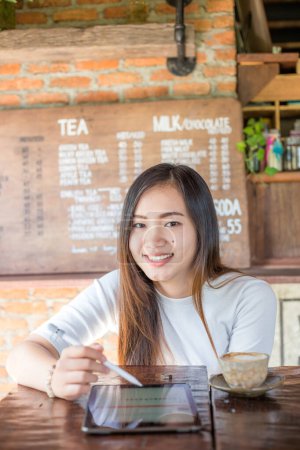 Téléchargez les photos : Belle jeune femme asiatique travaillant sur la tablette PC avec stylo électronique dans un café - en image libre de droit