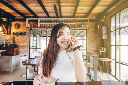 Téléchargez les photos : Femme d'affaires souriante parlant sur smartphone tenant tasse de café dans un café vintage - en image libre de droit