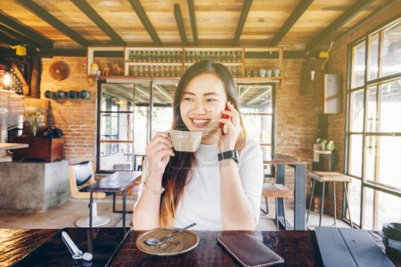 Photo for Smiling businesswoman talking on smartphone holding coffee cup in vintage cafe - Royalty Free Image