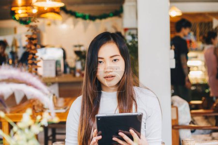 Téléchargez les photos : Belle jeune femme d'affaires assise au restaurant en utilisant une tablette numérique pc pour la communication - en image libre de droit