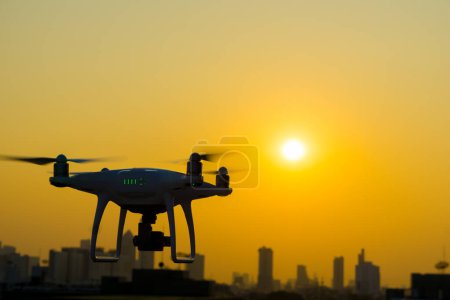 Téléchargez les photos : Silhouette de quadcopter survolant la ville au coucher du soleil - en image libre de droit