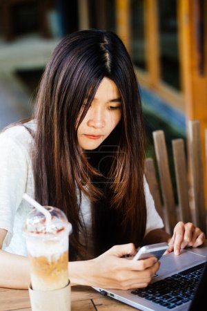 Téléchargez les photos : Femme d'affaires utilisant un ordinateur portable portable avec communication téléphonique tout en étant assis dans un café
. - en image libre de droit