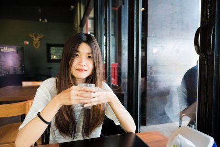 Téléchargez les photos : Jeune femme buvant un verre d'eau dans un café d'art après une boisson au café - en image libre de droit
