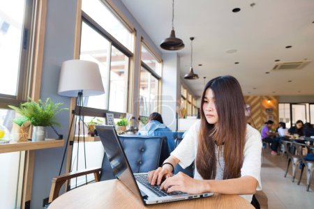Téléchargez les photos : Jeune étudiante intelligente apprenant sur ordinateur portable dans le café de la bibliothèque de l'université - en image libre de droit