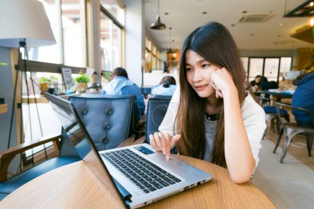 Téléchargez les photos : Souriant asiatique étudiant femme casual navigation sur internet dans café - en image libre de droit