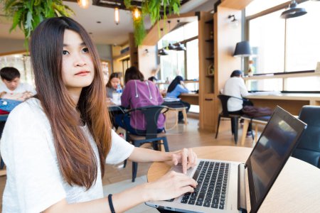 Téléchargez les photos : Jeune étudiante intelligente apprenant sur ordinateur portable dans le café de la bibliothèque de l'université - en image libre de droit