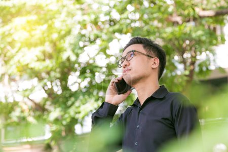 Foto de Hombre asiático con un teléfono en el parque al aire libre hablando por teléfono celular en un día soleado - Imagen libre de derechos