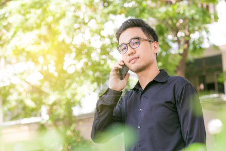 Foto de Hombre asiático con un teléfono en el parque al aire libre hablando por teléfono celular en un día soleado - Imagen libre de derechos