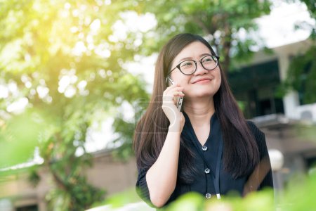 Photo for Portrait of a smiling beautiful asian woman talking with her phone in green park - Royalty Free Image