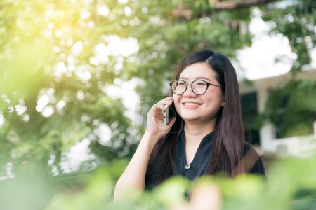 Téléchargez les photos : Heureuses lunettes asiatiques femme utilisent pour parler sur téléphone intelligent en plein air, Communication de la nature - en image libre de droit