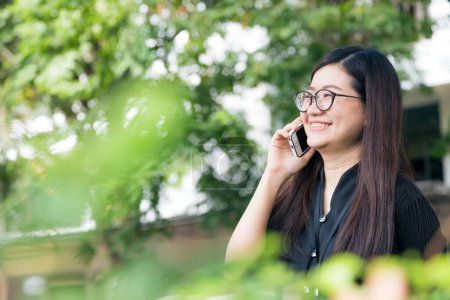 Foto de Feliz asiático gafas mujer uso a hablar en inteligente teléfono al aire libre, comunicación de la naturaleza - Imagen libre de derechos