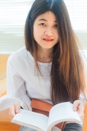 Foto de Retrato de una joven mujer asiática atractiva en la biblioteca sentada a leer un libro. Concepto educativo - Imagen libre de derechos