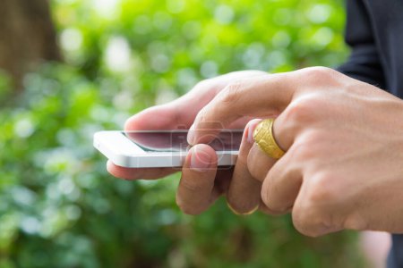 Téléchargez les photos : Business homme riche toucher sur téléphone portable à la main fermer fond d'herbe verte - en image libre de droit