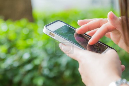 Téléchargez les photos : Main de femmes utilisant un téléphone intelligent mobile avec écran blanc blanc fond de parc vert - en image libre de droit
