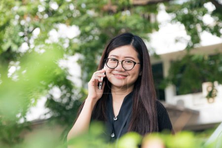 Téléchargez les photos : Lunettes asiatiques femmes d'affaires parlant téléphone portable dans le parc smilling pour le concept de succès - en image libre de droit