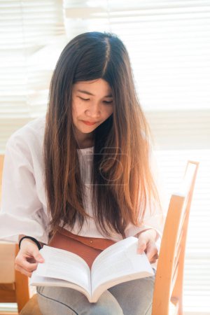 Photo for Happy asian student  young woman thinking with book in library sitting on wood table - Royalty Free Image