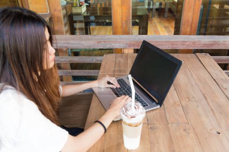Téléchargez les photos : Belle étudiante hipster utilisant un ordinateur portable et buvant du café au café - en image libre de droit