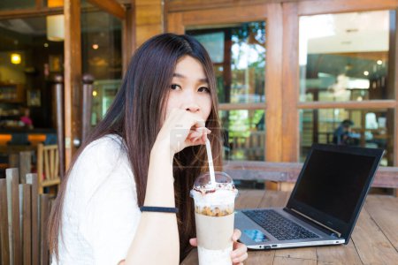 Téléchargez les photos : Belle étudiante hipster utilisant un ordinateur portable et buvant du café au café - en image libre de droit