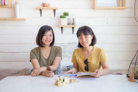 Téléchargez les photos : Heureux asiatique femme ami assis dans café commander un verre à la recherche dans menu relation concept - en image libre de droit