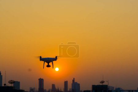 Téléchargez les photos : Silhouette quadcopter volant sur le coucher du soleil bâtiment de la ville - en image libre de droit