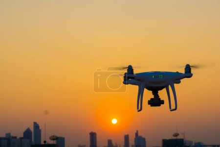 Téléchargez les photos : Silhouette quadcopter volant sur le coucher du soleil bâtiment de la ville - en image libre de droit