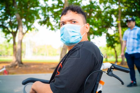 Photo for Disabled man sitting in a wheelchair wear mask enjoying in the public park with mom outdoor vacation - Royalty Free Image
