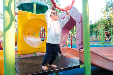 Téléchargez les photos : Garçon heureux jouissant avec aire de jeux extérieure dans le parc de la ville - en image libre de droit