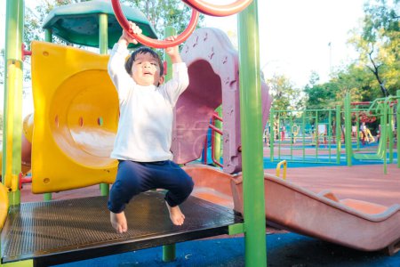 Téléchargez les photos : Garçon heureux jouissant avec aire de jeux extérieure dans le parc de la ville - en image libre de droit
