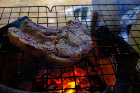 Téléchargez les photos : Steak de porc placé sur une grille de barbecue au-dessus d'une flamme brûlante - en image libre de droit
