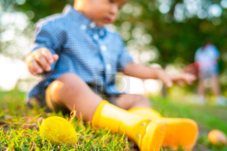 Téléchargez les photos : Heureux asiatique garçon avec Pâques oeuf sur vert herbe pelouse jaune chaussure de démarrage dans ville parc coucher de soleil lumière - en image libre de droit
