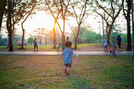 Foto de Feliz alegre niño asiático 2 año niño jugando en ciudad público parque puesta del sol caliente luz al aire libre actividad - Imagen libre de derechos