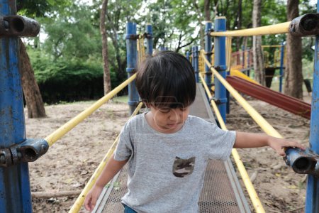 Téléchargez les photos : Heureux préscolaire asiatique garçon appréciant avec plein air curseur dans ville parc aire de jeux - en image libre de droit