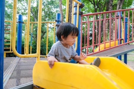 Téléchargez les photos : Heureux préscolaire asiatique garçon appréciant avec plein air curseur dans ville parc aire de jeux - en image libre de droit