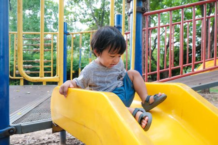 Photo for Happy preschool asian boy enjoying with outdoor slider in city park playground - Royalty Free Image