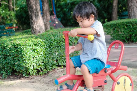 Téléchargez les photos : Préscolaire asiatique garçon appréciant avec vélo jouet équipement dans ville aire de jeux parc ensoleillé jour - en image libre de droit