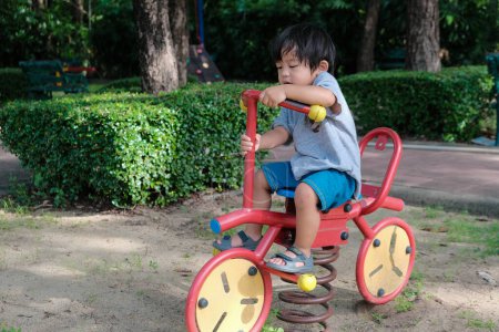 Photo for Preschool asian boy enjoying with bike toy equipment in city playground park sunny day - Royalty Free Image