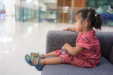 Foto de Adorable 2 año asiático chica sentado en acogedor sofá en hospital borrosa fondo concepto de atención médica - Imagen libre de derechos