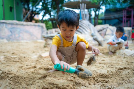 Téléchargez les photos : Jardin d'enfants asiatique de 5 ans jouant dans un bac à sable s'amusant sur une aire de jeux dans un bac à sable. Activités créatives extérieures - en image libre de droit